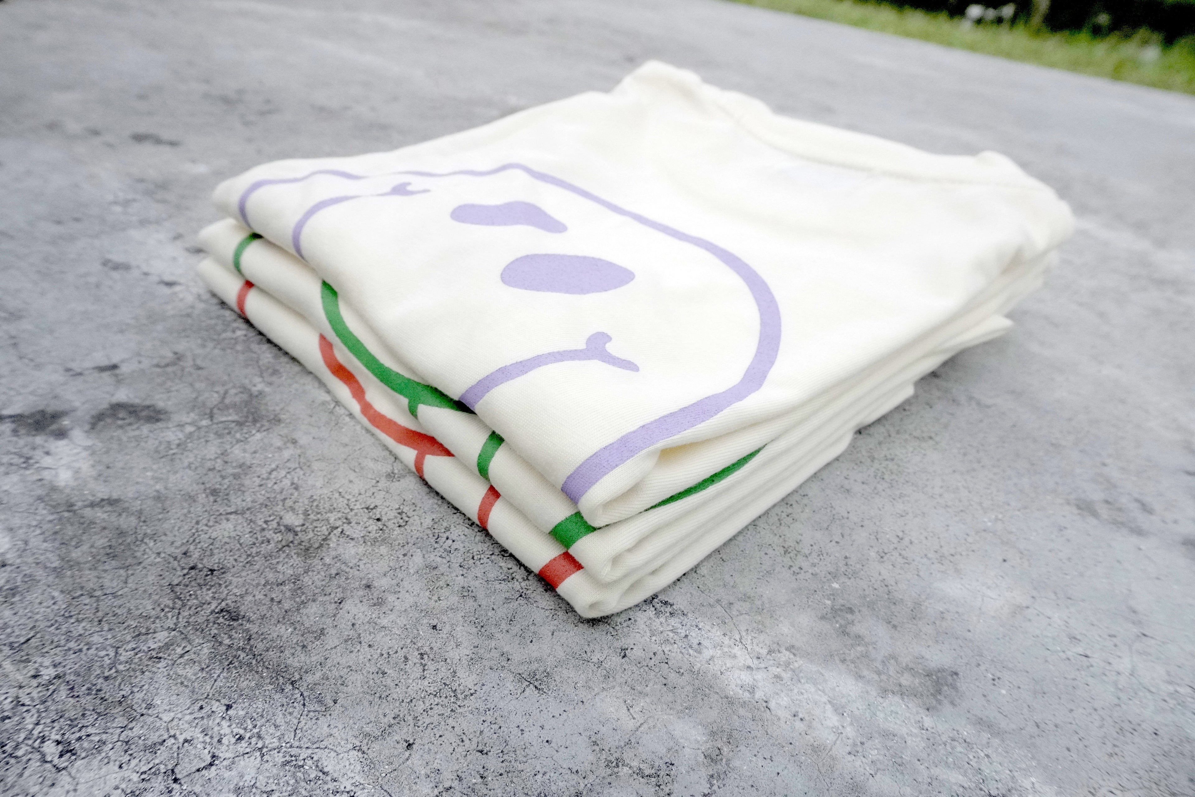 Stack of white tees for toddlers with colorful designs on a gray surface